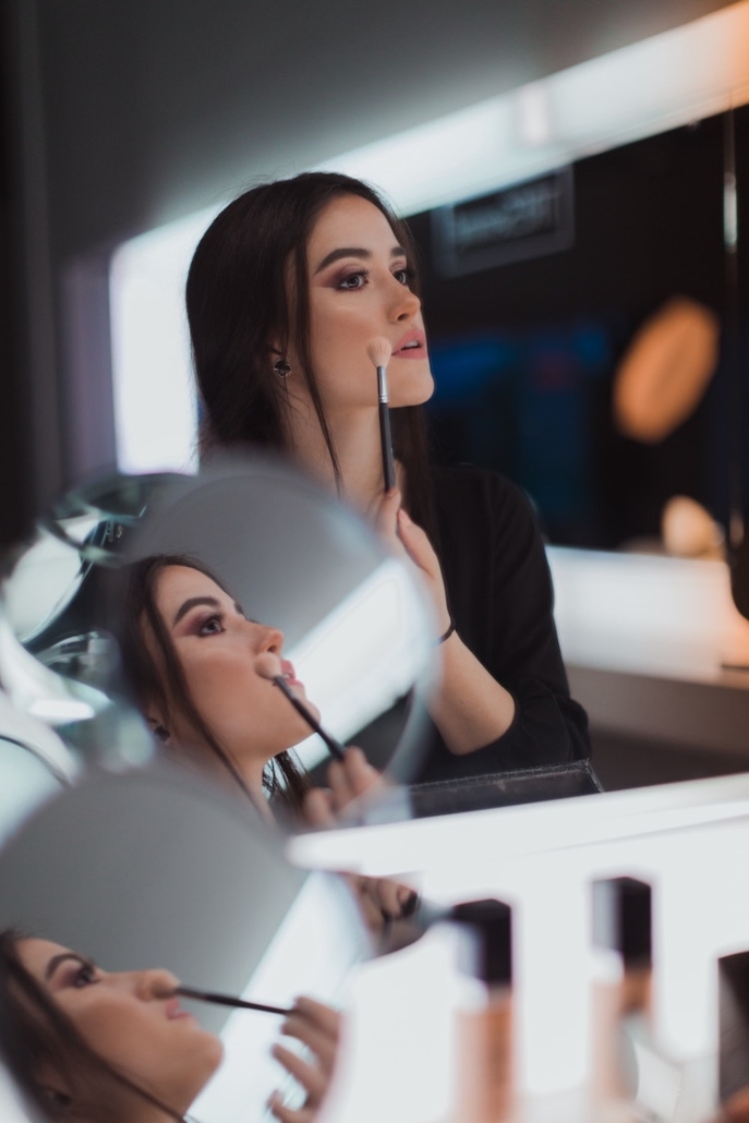 girl applies makeup in front of mirror