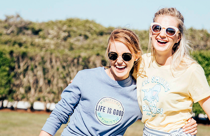 Two women wearing Life Is Good t-shirt holding each other in sunlight