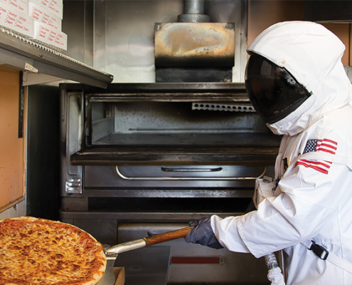 Man in astronaut suit taking pizza out of oven