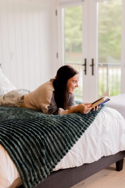 Editor reading on bed covered in a Bedsure velvet throw blanket at CBC's Holiday House in Stowe, Vermont